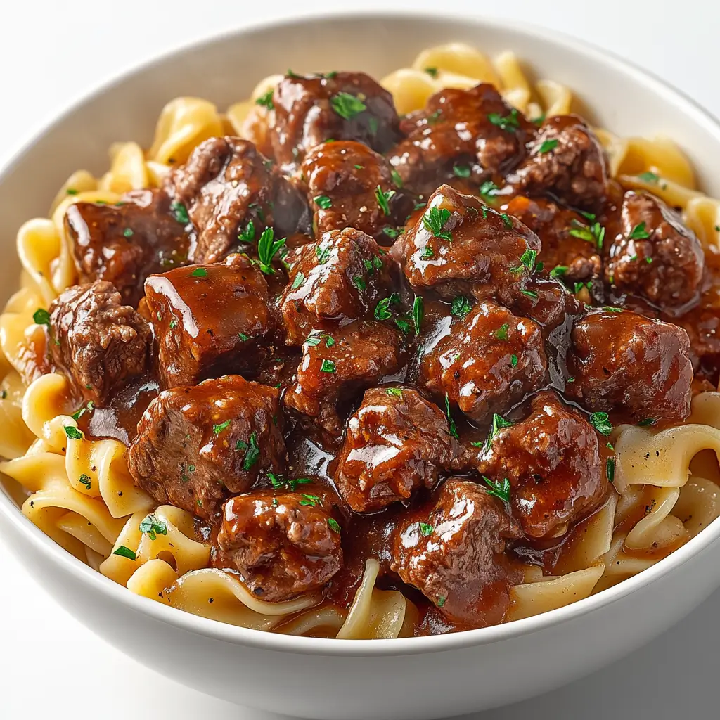 Slow-cooked beef tips and noodles in rich brown gravy, garnished with parsley.